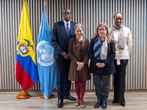 Un hombre y tres mujeres posan para una foto de grupo institucional al lado de las bandares de Colombia y de la ONU.