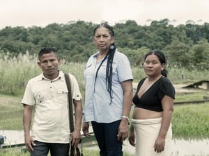 Un hombre y dos mujeres frente a un arroyo al borde de una selva tropical.
