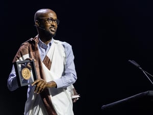 Un hombre somalí, que usa anteojos y viste un traje tradicional, sonríe mostrando la medalla que recibió por haber sido electo ganador global del Premio Nansen