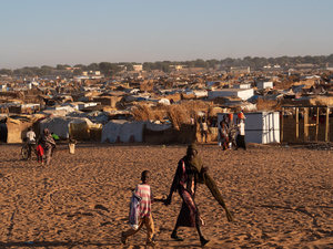 Tomados de la mano, una mujer y un niño caminan frente a un asentamiento de refugiados