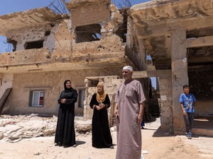 Siria. Un grupo de personas de pie delante de los escombros de una vivienda dañada por bombardeos.