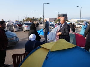 En un estacionamiento al aire libre convertido en campamento de tiendas de campaña varias personas conversan al lado de una carpa.