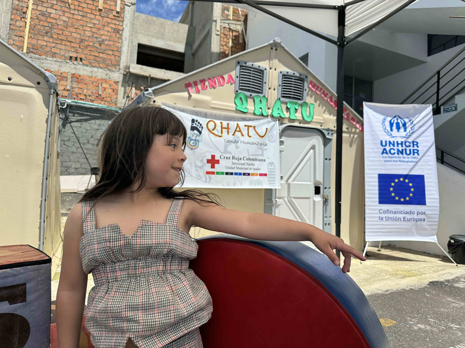 Una niña juega en un espacio infantil en un punto de atención. Detrás de ella se observa un rotúlo con la bandera de la Unión Europea.