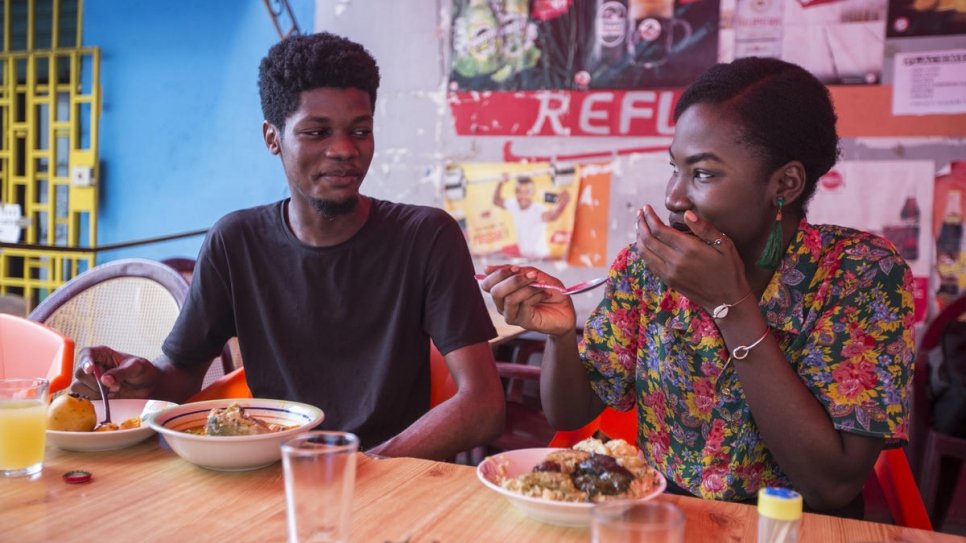 O designer gráfico da Costa do Marfim O’Plérou desfruta de uma refeição tradicional com um amigo em uma lanchonete popular de Abidjan, Costa do Marfim