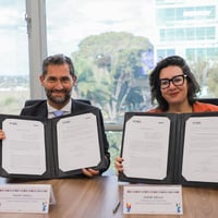 Representante do ACNUR e Ministra dos Direitos Humanos no Brasil estão sentados segurando um acordo assinado nas mãos e sorrido para a foto
