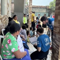 Equipe do ACNUR realiza atendimento e coleta de informações junto a famílias deslocadas em área residencial, enquanto crianças e adultos aguardam atendimento.
