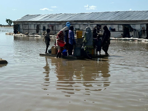 Um grupo de pessoas tenta ligar uma fonte de água potável, no meio de uma paisagem inundada.