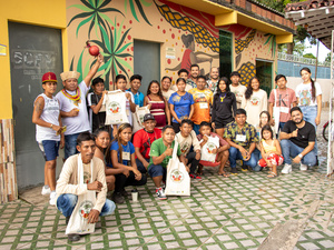 Grupo de pessoas posando em frente a um mural colorido com desenhos abstratos e a figura de uma pessoa segurando um objeto. 