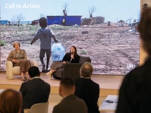 Duas mulehres sentadas em apresentação de painel diante de plateia.