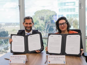 Representante do ACNUR e Ministra dos Direitos Humanos no Brasil estão sentados segurando um acordo assinado nas mãos e sorrido para a foto