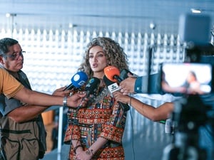 Mulher refugiada concede entrevista a jornalistas, cercada por vários microfones com logotipos de emissoras e câmera de gravação