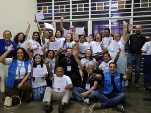 Grupo de participantes do programa Empretec para Refugiados posa com certificados ao final da capacitação, acompanhado por representantes de organizações parceiras, em sala de treinamento.