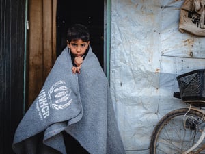 Menino se aquece num abrigo no campo de refugiados de Za’atari, na Jordânia, usando cobertores e aquecedores fornecidos pelo ACNUR