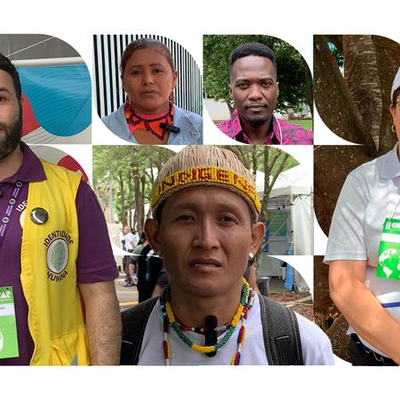 Seis pessoas com os rostos desfocados usam crachás verdes e brancos. Elas estão vestidas de formas variadas, algumas com uniformes ou roupas coloridas. Ao fundo, há árvores e estruturas, sugerindo um ambiente ao ar livre ou um evento.