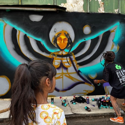 Menina de costas observa uma artista mulher pintando uma parede