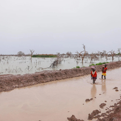 Pessoas deslocadas pelas enchentes carregam crianças e pertences ao longo de uma estrada alagada em Bentui, Sudão do Sul, em julho de 2024.