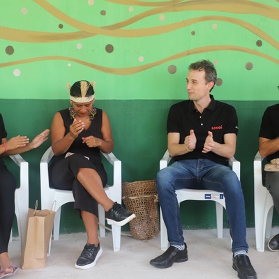 Quatro pessoas sentadas frente a uma parede colorida aplaudem e sorriem