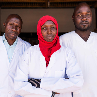 Três jovens vestidos de jaleco branco. Os refugiados sudaneses Hassan Zakaira, Fatima Abdolgadir e Yacoub Idriss são profissionais de saúde originários de Darfur Ocidental, no Sudão, e atualmente trabalham em um hospital no campo de refugiados de Aboutengue, no Chade. 