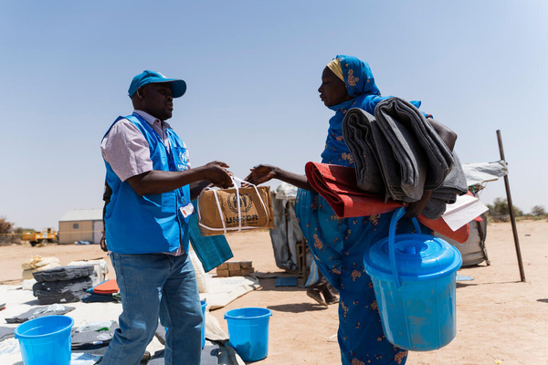 Funcionário do ACNUR entrega itens de ajuda humanitária a mulher no Chade. Milhares de refugiados sudaneses continuam a fugir através da fronteira.
