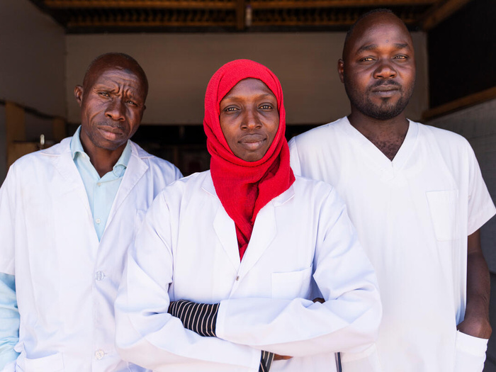 Três jovens vestidos de jaleco branco. Os refugiados sudaneses Hassan Zakaira, Fatima Abdolgadir e Yacoub Idriss são profissionais de saúde originários de Darfur Ocidental, no Sudão, e atualmente trabalham em um hospital no campo de refugiados de Aboutengue, no Chade. 