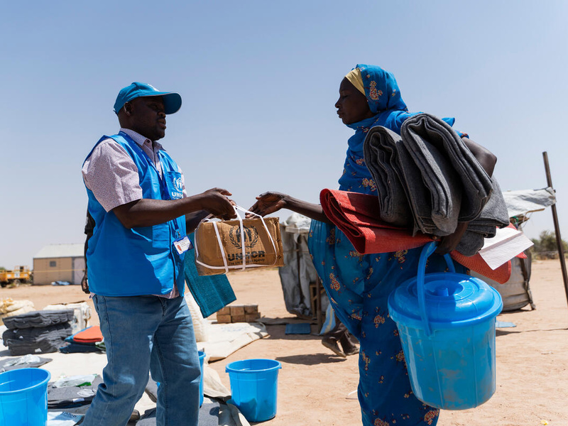 Funcionário do ACNUR entrega itens de ajuda humanitária a mulher no Chade. Milhares de refugiados sudaneses continuam a fugir através da fronteira.