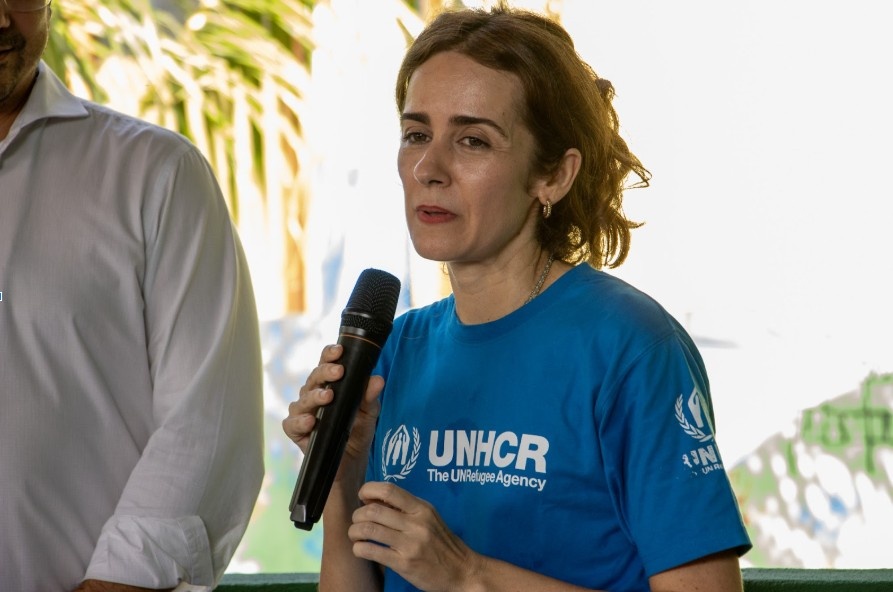 Mulher de camiseta azul com logo do ACNUR fala ao microfone