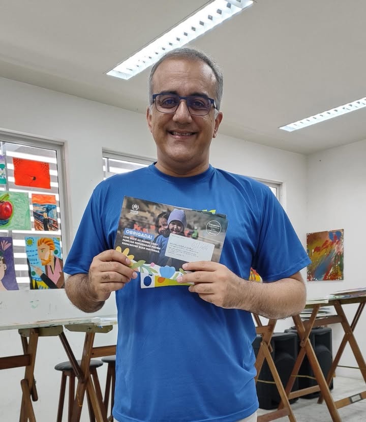 Homem de camiseta azul mostra carta enviada a doadores do ACNUR