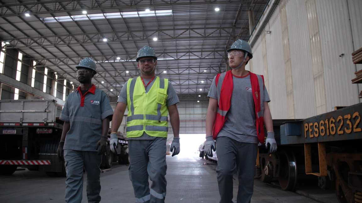 Profissionais com equipamentos de seguran&ccedil;a caminhando em armaz&eacute;m industrial com caminh&otilde;es de carga