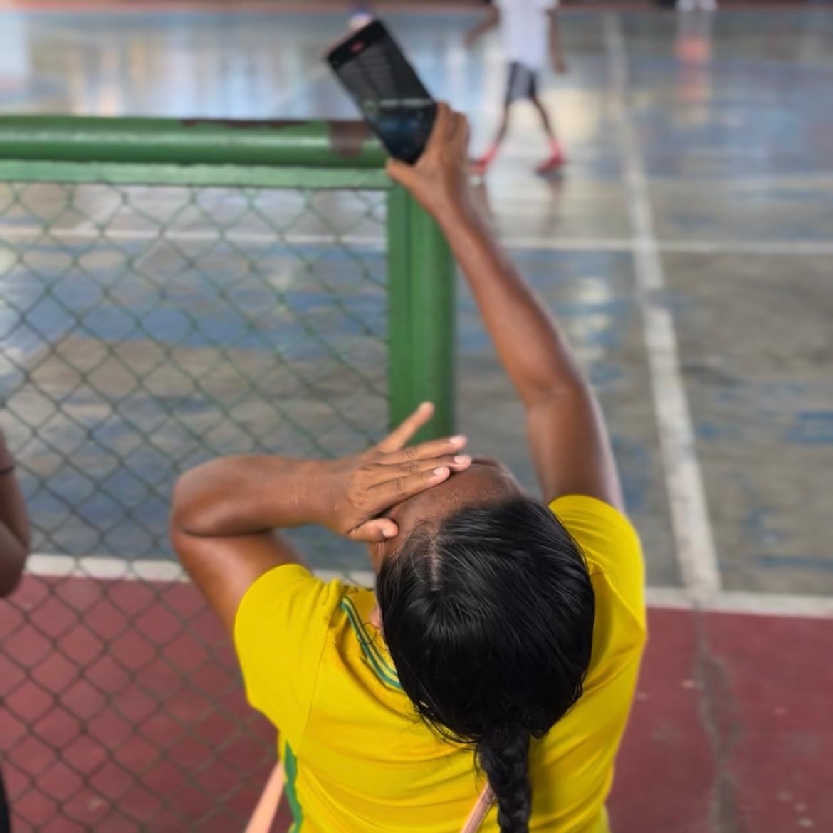 Mulher ind&iacute;gena venezuelana de camiseta amarela segura um celular na m&atilde;o direita e com a m&atilde;o esquerda na testa, torcedora sofre pela partida de futebol
