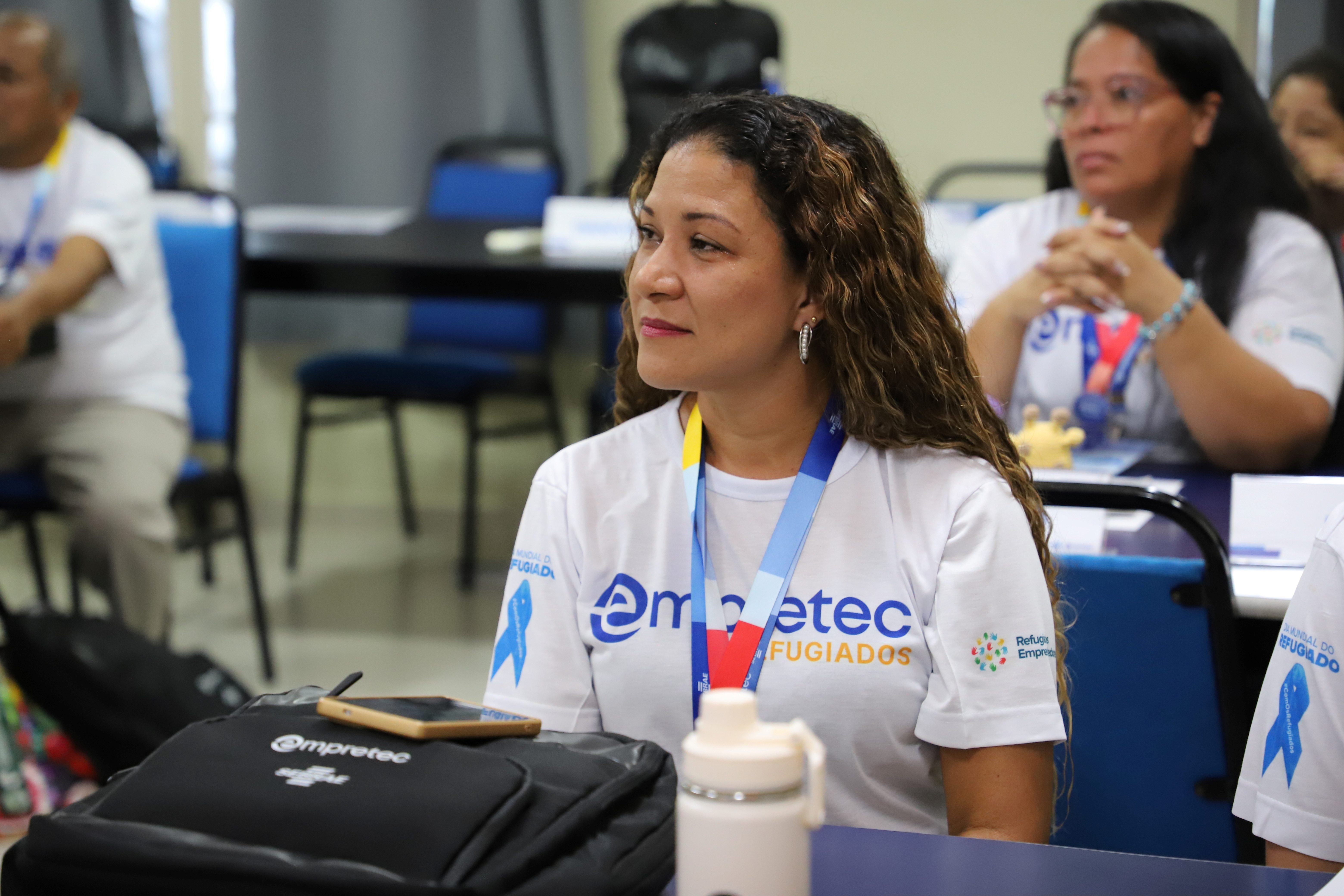 Aluna do programa Empretec para Refugiados acompanha atividade de capacita&ccedil;&atilde;o em sala de aula, usando camiseta do projeto e crach&aacute; de identifica&ccedil;&atilde;o.