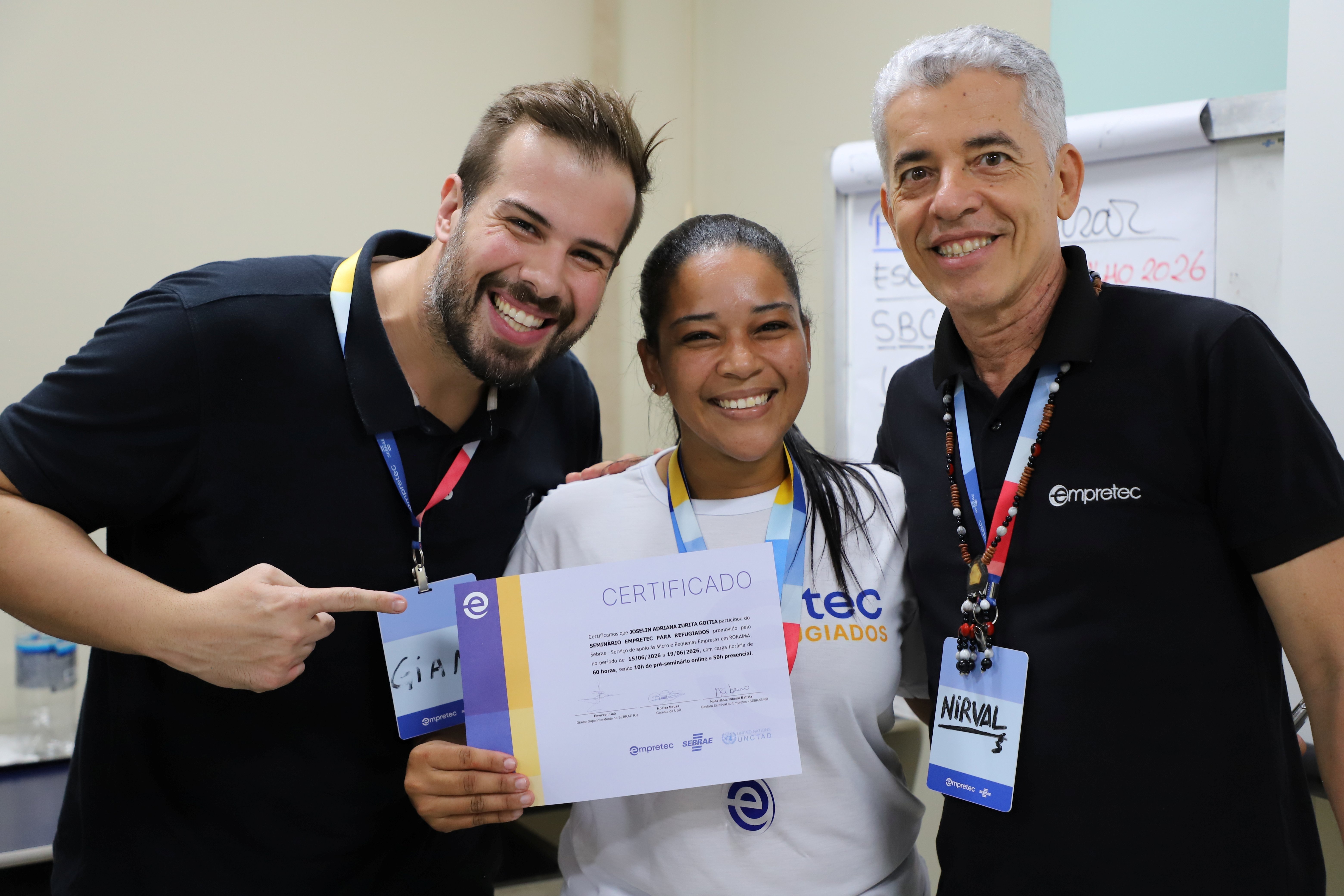 Participante do programa Empretec para Refugiados exibe certificado de conclus&atilde;o ao lado de facilitadores durante cerim&ocirc;nia de encerramento da capacita&ccedil;&atilde;o.