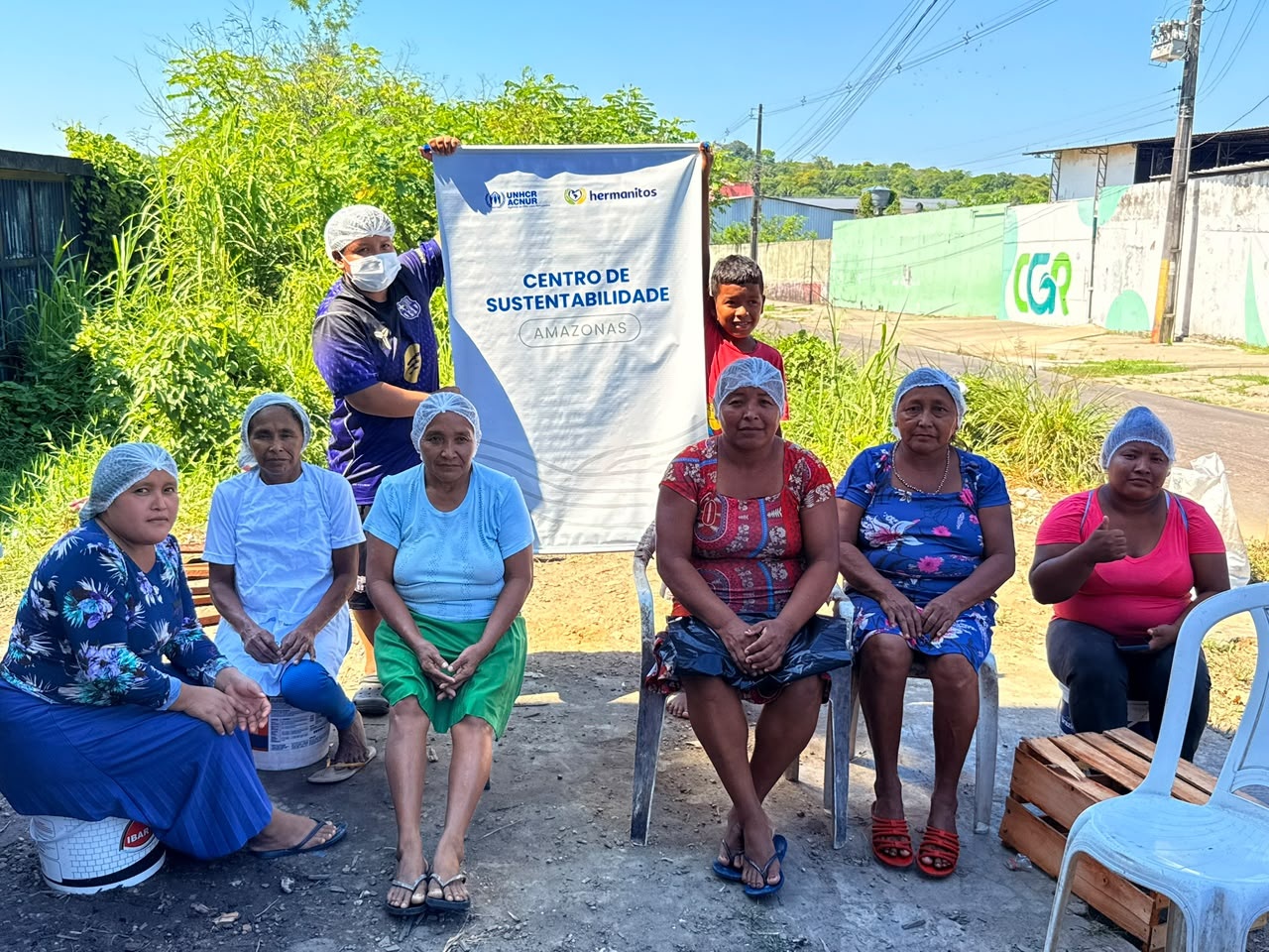 Grupo de mulheres ind&iacute;genas Warao se re&uacute;ne em &aacute;rea comunit&aacute;ria durante atividade das Brigadas Ecol&oacute;gicas. Ao fundo, um banner do Centro de Sustentabilidade Amazonas, iniciativa apoiada pelo ACNUR e parceiros.