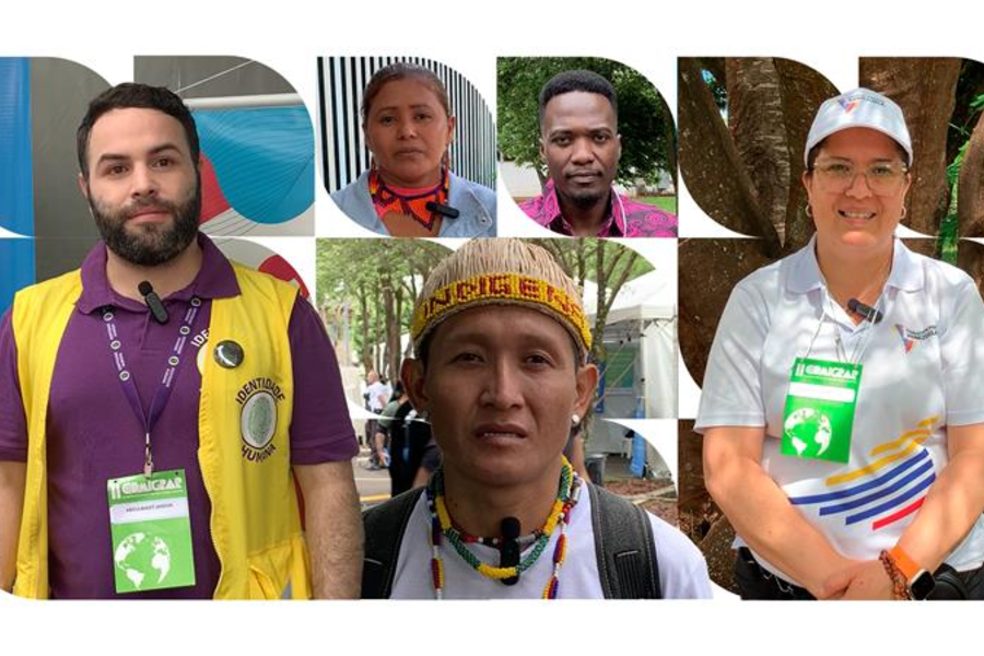 Seis pessoas com os rostos desfocados usam crachás verdes e brancos. Elas estão vestidas de formas variadas, algumas com uniformes ou roupas coloridas. Ao fundo, há árvores e estruturas, sugerindo um ambiente ao ar livre ou um evento.