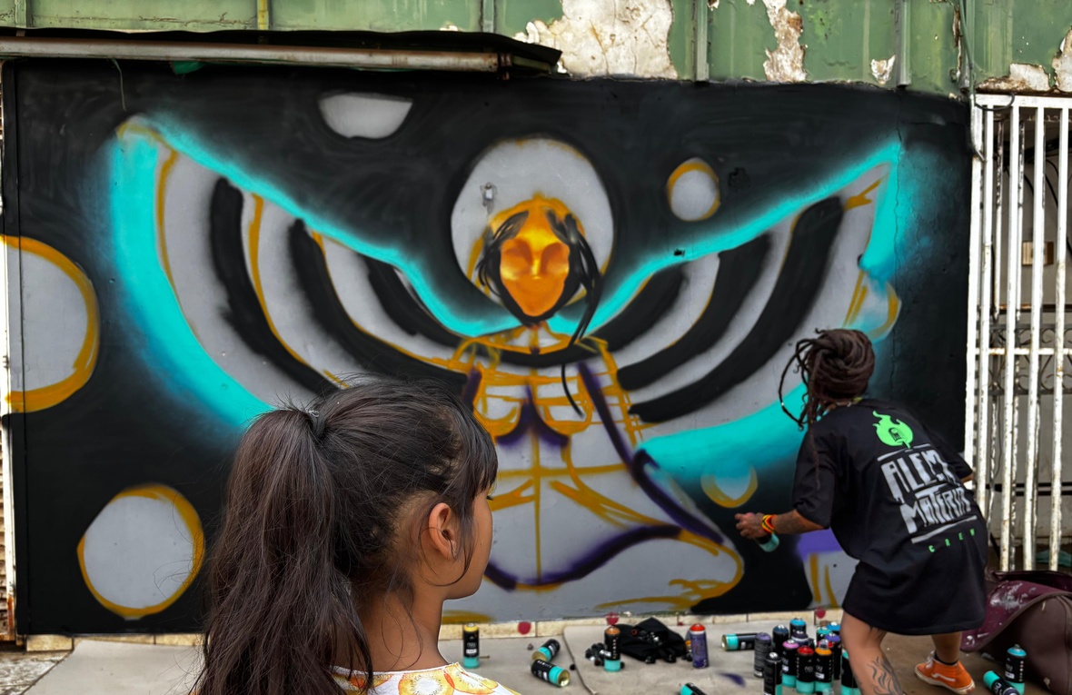 Menina de costas observa uma artista mulher pintando uma parede
