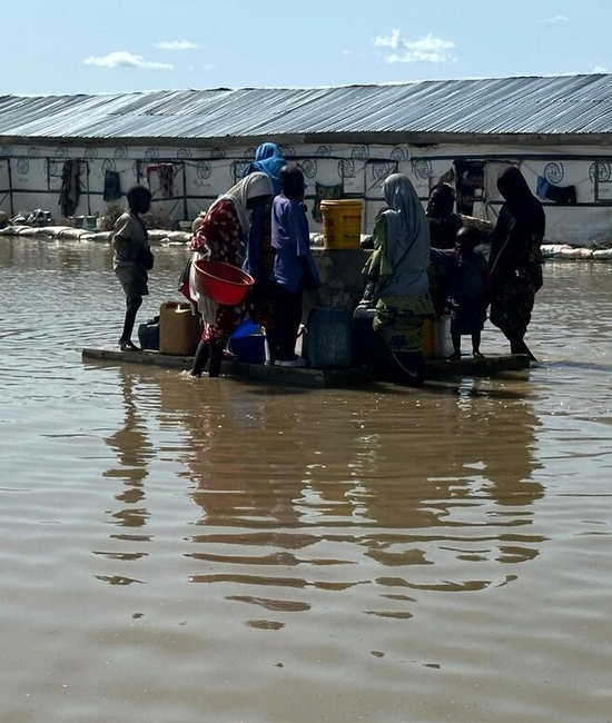 Um grupo de pessoas tenta ligar uma fonte de água potável, no meio de uma paisagem inundada.