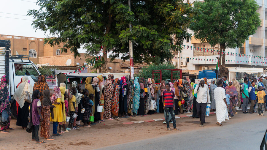 Famílias recentemente deslocadas de El Fasher fazem fila para distribuição de alimentos ao lado de moradores de longa data em Omdurman, a segunda maior cidade do Sudão. 