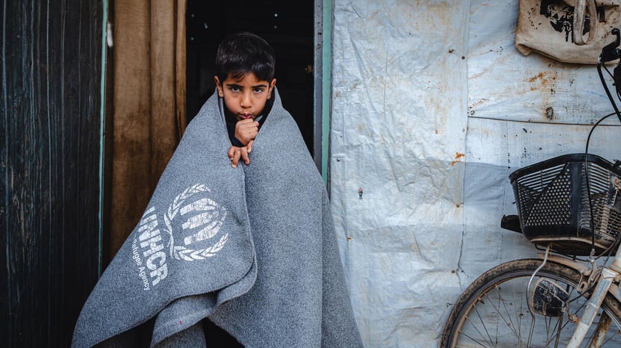 Menino se aquece num abrigo no campo de refugiados de Za’atari, na Jordânia, usando cobertores e aquecedores fornecidos pelo ACNUR