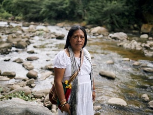 Mujer indígena frente cámara y atrás un río 