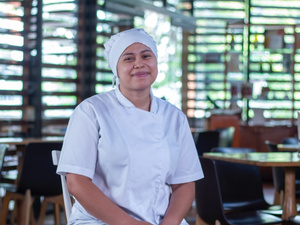 Mujer joven sonríe frente a cámara con indumentaria de cocina 
