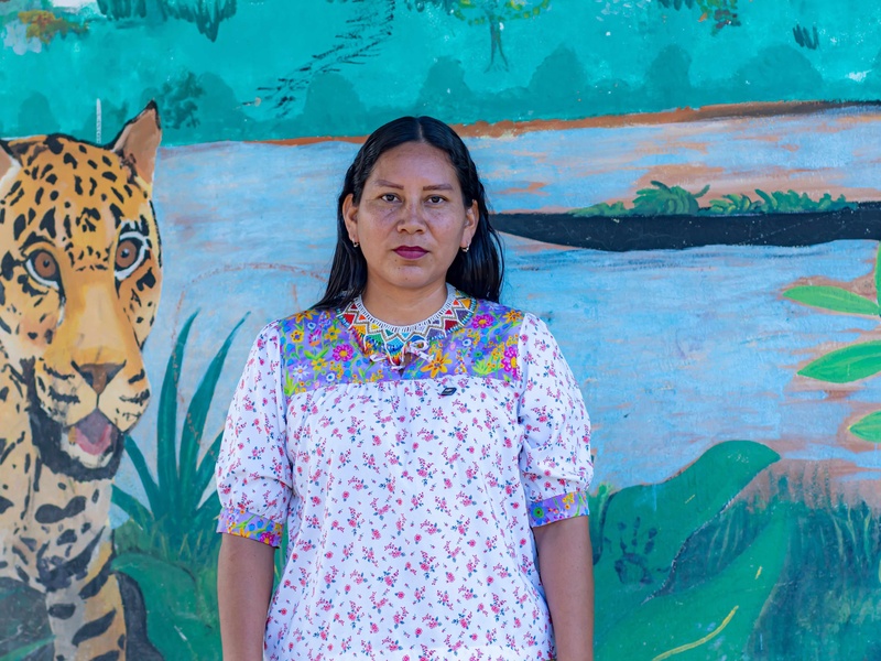 Mujer indígena Siona a su respaldo mural colorido con un jaguar 