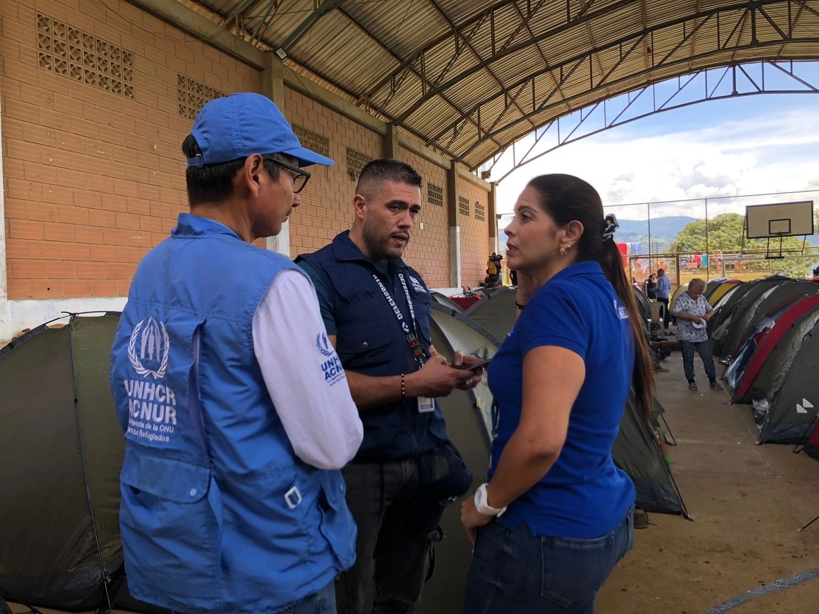 Personal de ACNUR y otros funcionarios conversan en el fondo se observa carpas de emergencia 