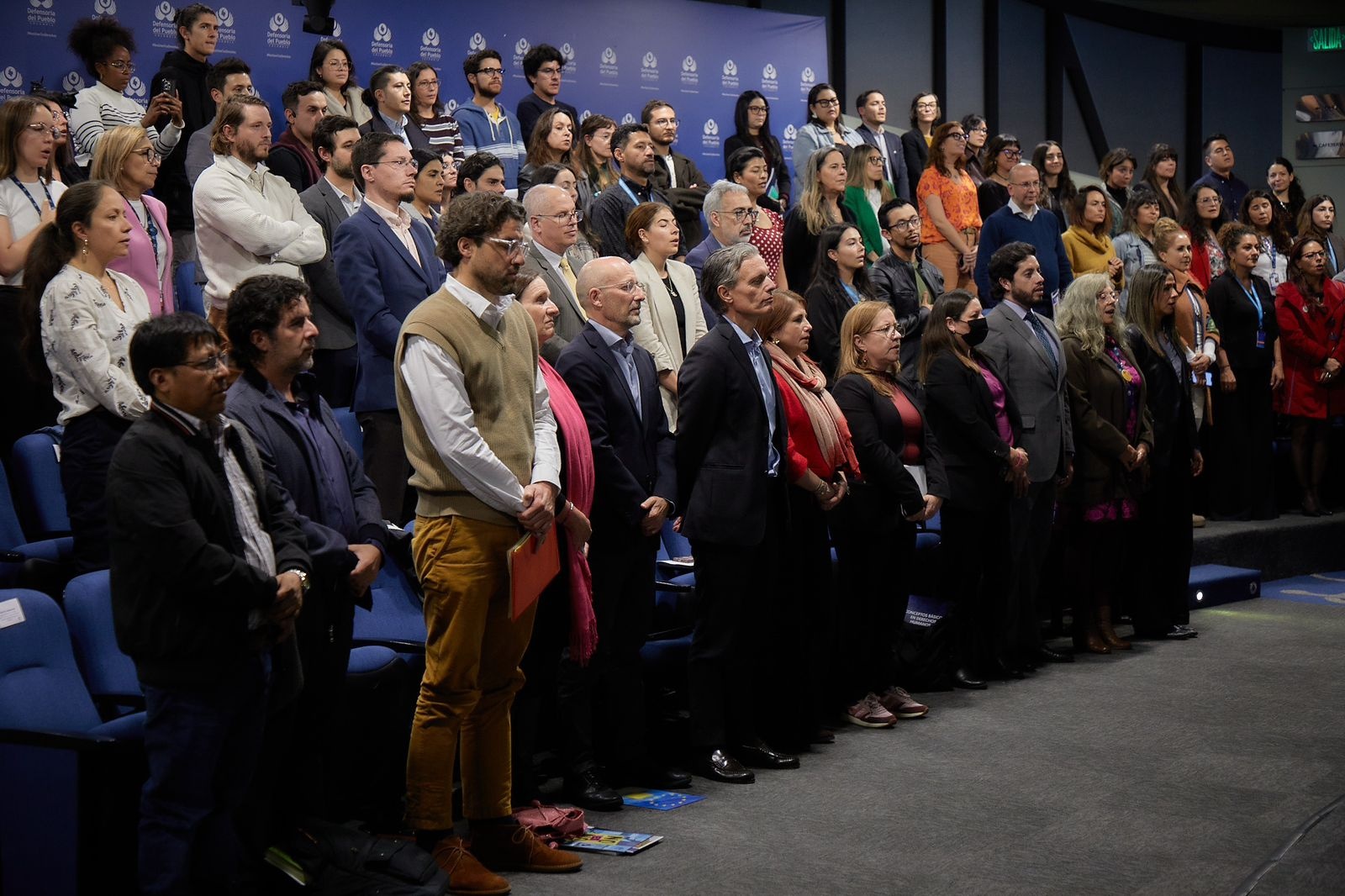 Participantes de pie en el auditorio de la sede nacional de la Defensoría del Pueblo. 