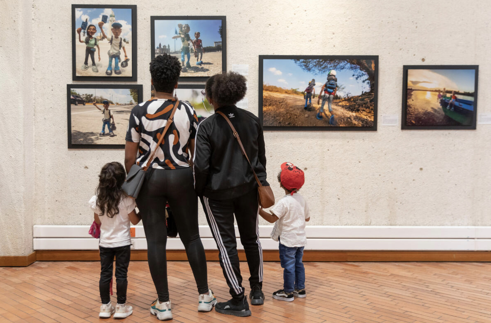 Asistentes a la exposición Refugiados y Migrantes dos mujeres adultas y un niño y una niña frente las fotografías. 