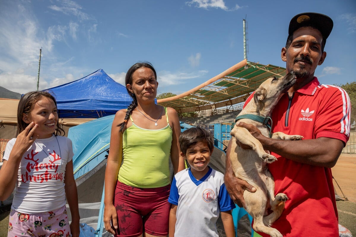 Una mujer y dos niños están de pie fuera de una tienda de campaña junto a un hombre que sostiene a un perro