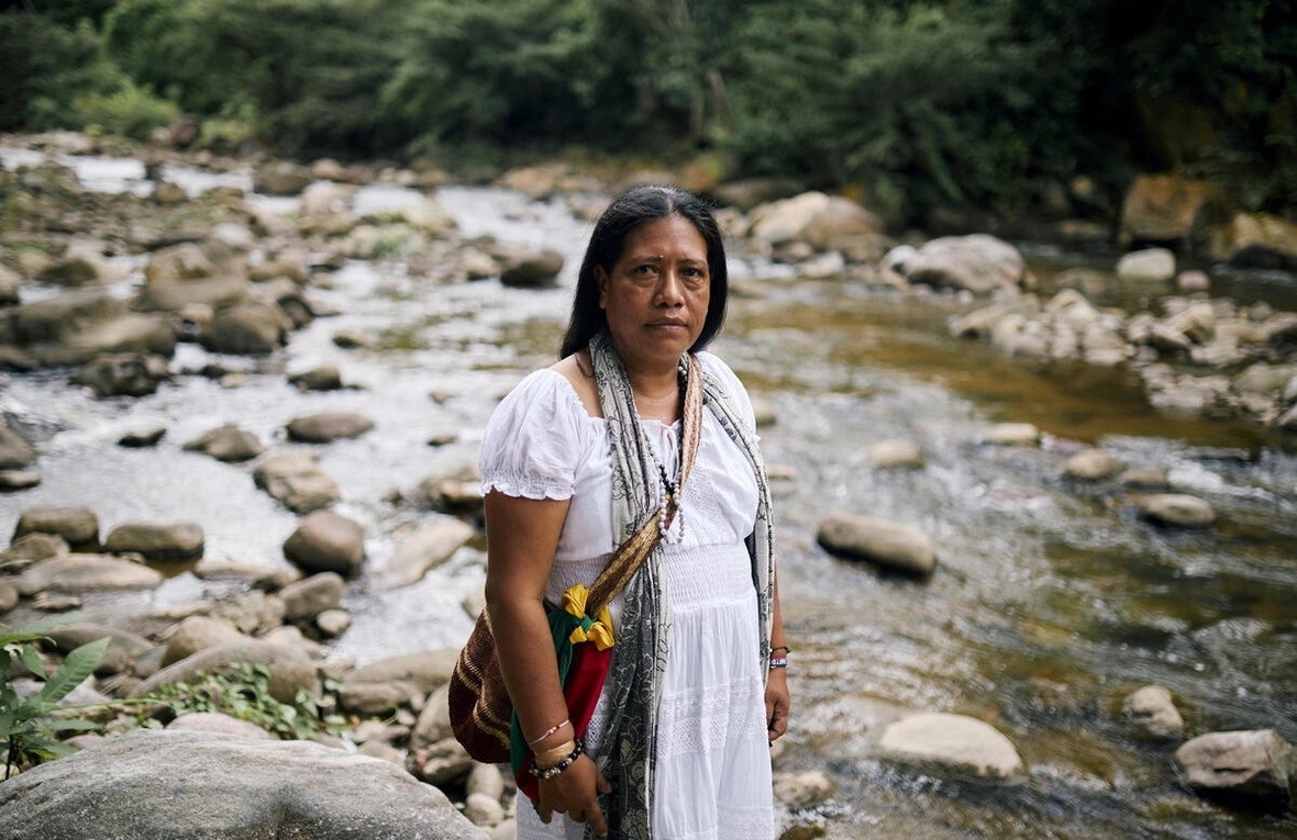 Mujer indígena frente cámara y atrás un río 