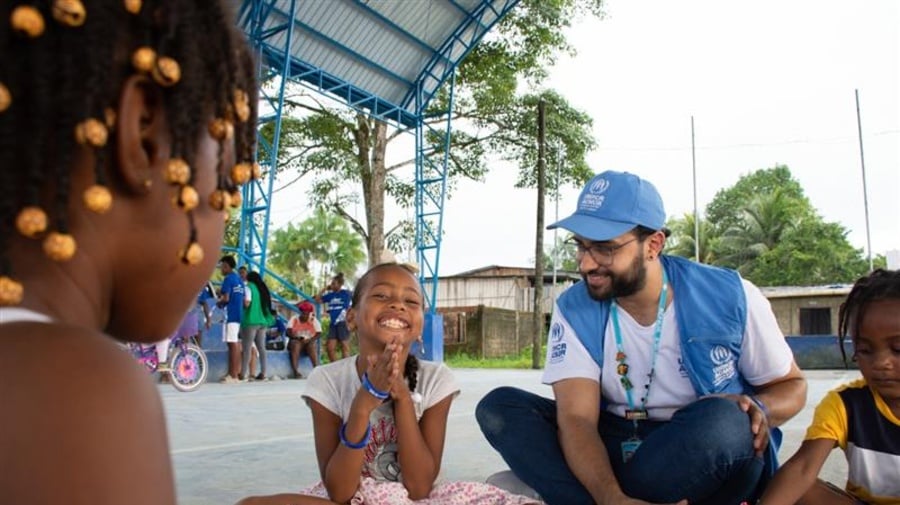 Un grupo de niñas y niños juegan en una actividad comunitaria acompañados por un trabajador de ACNUR.