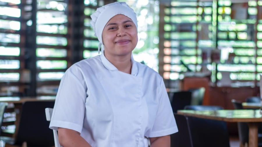 Mujer joven sonríe frente a cámara con indumentaria de cocina 