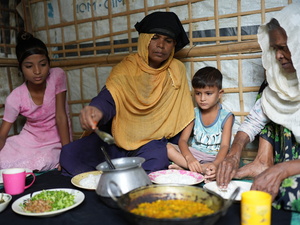 Una madre y una abuela comen sentadas en el suelo de su alojamiento con dos niños pequeños.