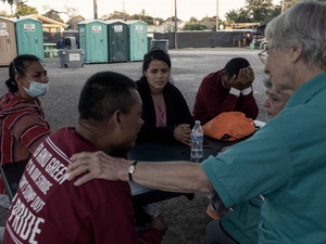Una trabajadora humanitaria sentada en un estacionamiento con cinco personas en necesidad.