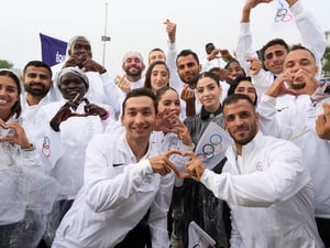 Un grupo de jóvenes vestidos con prendas deportivas blancas forman con los dedos emojis de corazones.